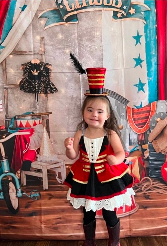 Little girl in a red and black ringmaster outfit in front of a circus backdrop