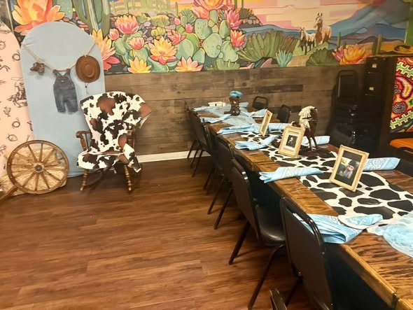 Long cowboy baby shower table with cow print runners in front of a desert mural