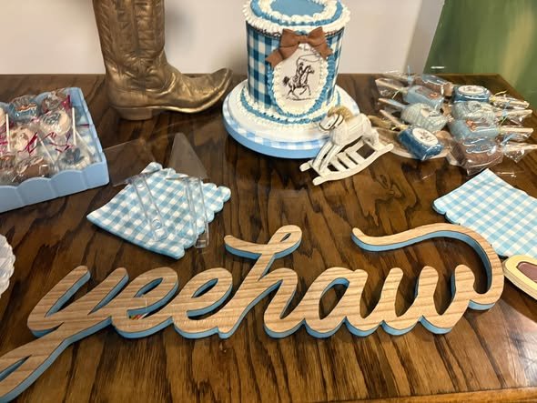 Wood Yeehaw sign in front of a cowboy cake, cowboy boot and blue gingham napkins