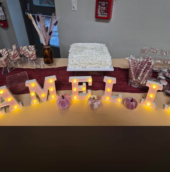 Light up name letters in front of a baby shower cake with pumpkins