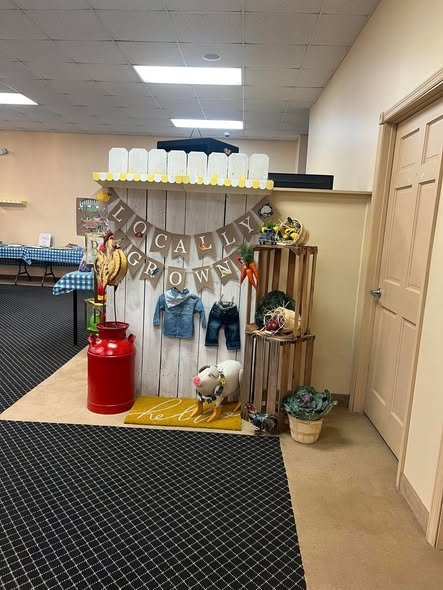 Farmers market baby shower corner with wood crates, baby clothes and a red milk can