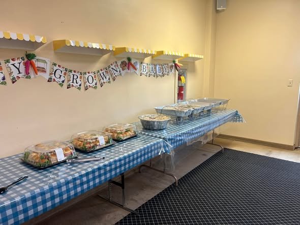 Long baby shower food table with blue gingham and a Baby Grown banner
