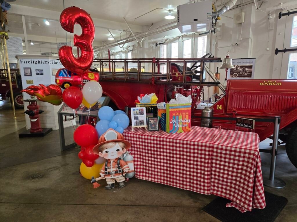 Party hall with a vintage fire truck, a red gingham table and a balloon column with a number 3