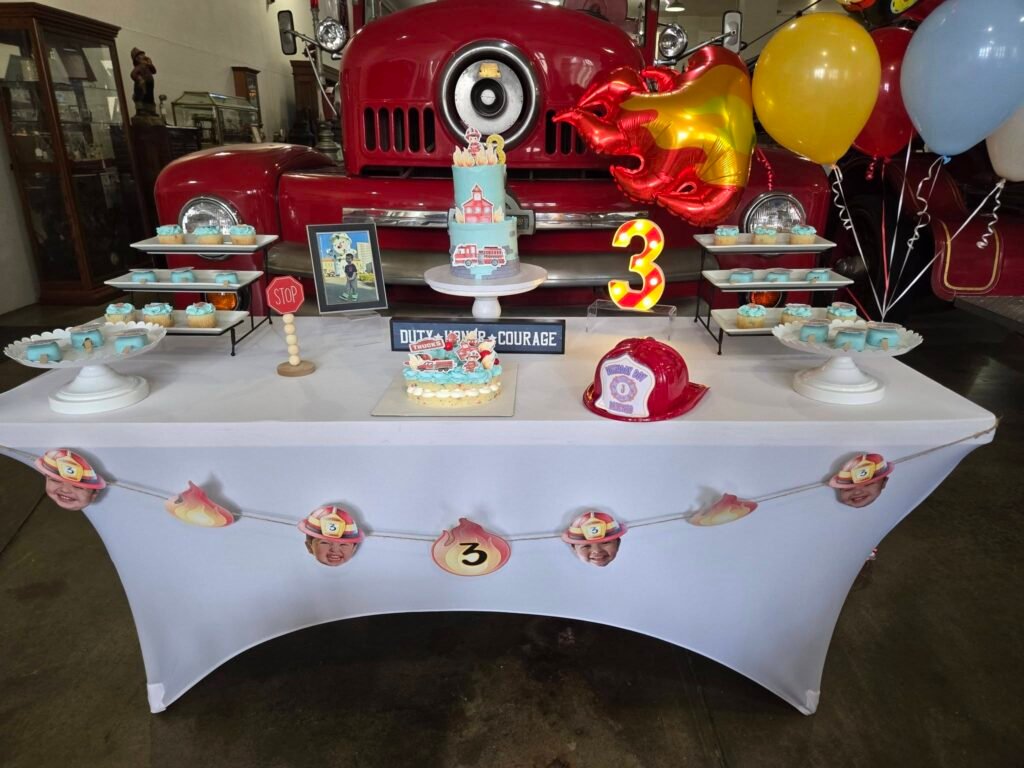 Fire truck birthday cake table in front of a vintage red fire truck with a number 3 balloon