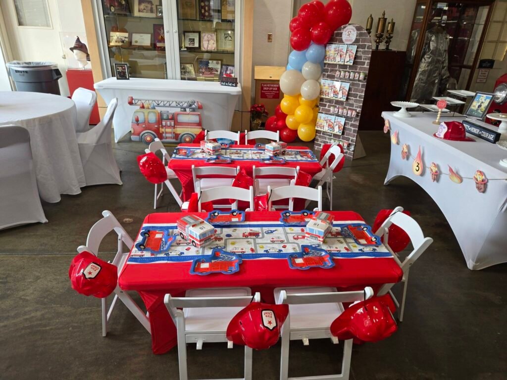 Wide view of kids tables with red fire hats and balloon columns