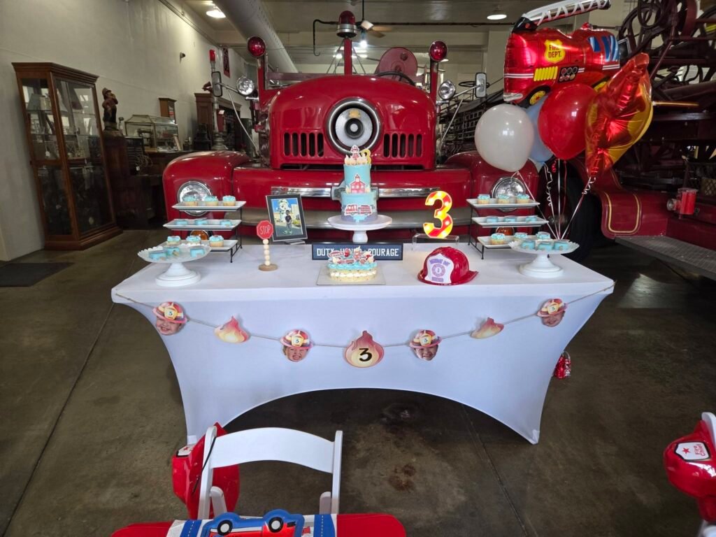 Cake table with firefighter bunting and a fire hat in front of the fire truck