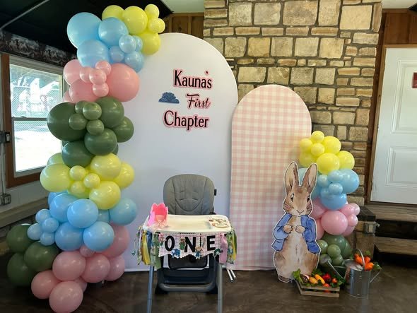 First Chapter 1st birthday backdrop with pastel balloons, a Peter Rabbit cutout and a high chair with a ONE banner