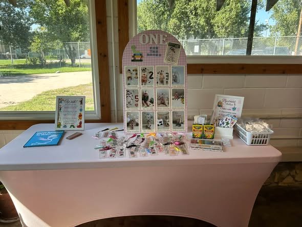 First year photo board on a table with books and party favors