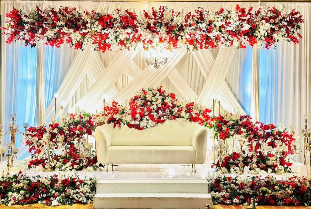 Wedding stage with a cream sofa, white drapes and red flowers