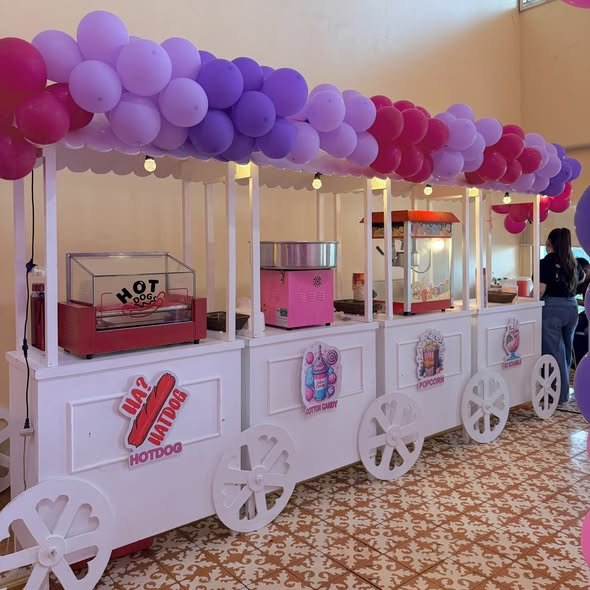 Row of white party food carts with hotdog, cotton candy and popcorn machines under a purple balloon canopy