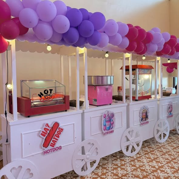Side view of white hotdog and cotton candy carts with a pink and purple balloon garland