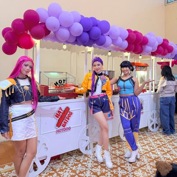 Costumed characters posing in front of party food carts with a purple balloon canopy