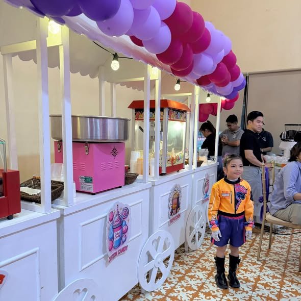 Child in a costume posing by party food carts with a balloon canopy
