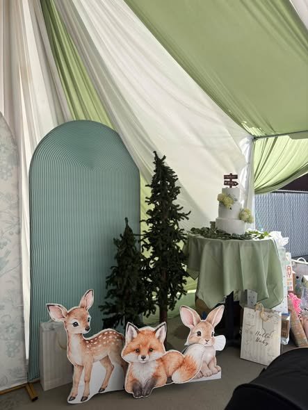 Sage arch with small pine trees and deer cutouts next to the cake table