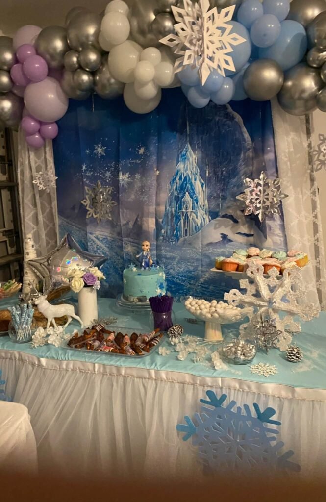 Frozen castle backdrop behind a dessert table with snowflakes and balloons