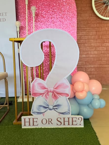 Question mark sign with a bow next to pink glitter panels and balloons