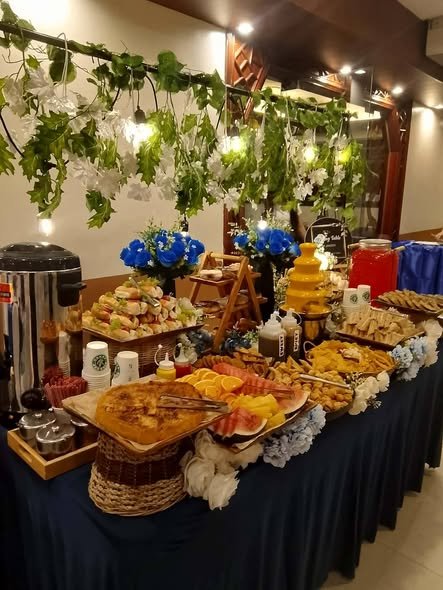 Grazing table with wood risers, pastries and a drink dispenser under hanging greenery