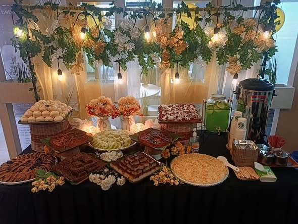 Grazing table with trays of snacks, a juice dispenser and a greenery and light canopy