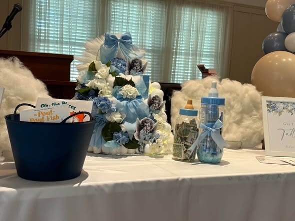 Blue baby shower gift table with cloud decor, a diaper cake and a gift tub