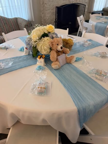 Teddy bear centerpiece with white and blue flowers on a blue table runner