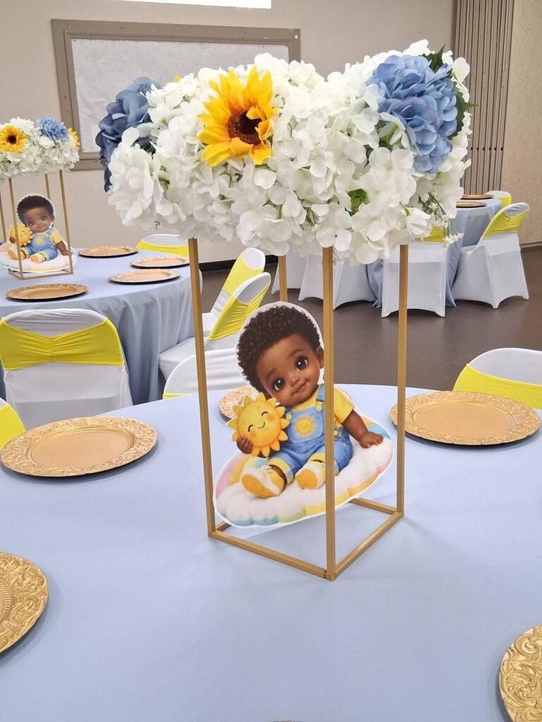 Tall gold frame centerpiece with sunflowers, white flowers and blue hydrangeas over a baby cutout