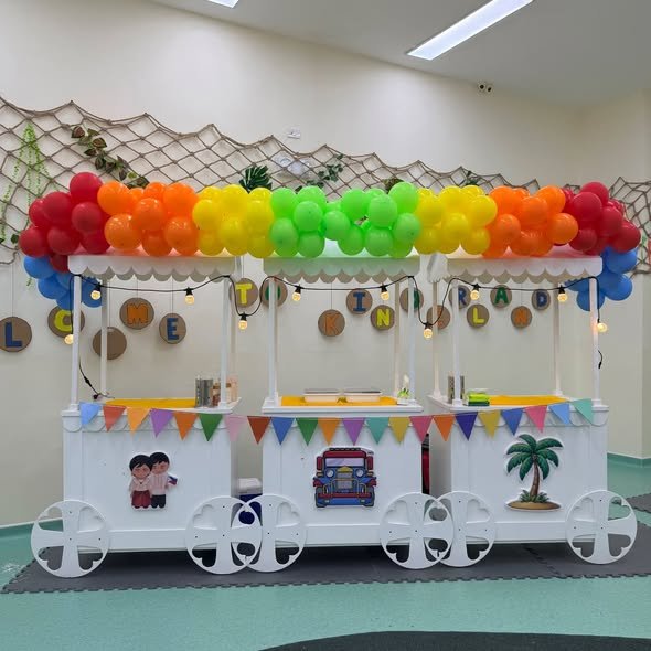 Row of white party carts with a rainbow balloon canopy and colorful bunting