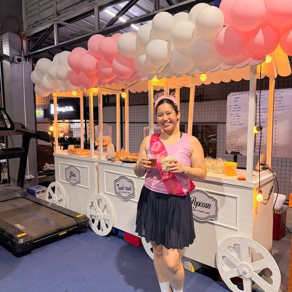 Guest holding a drink by a white cart with a pink and white balloon canopy