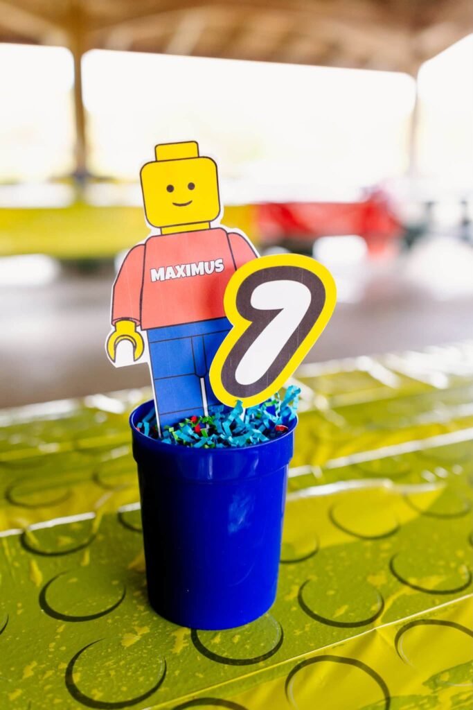 LEGO minifigure and number 7 centerpiece in a blue cup on a green baseplate tablecloth