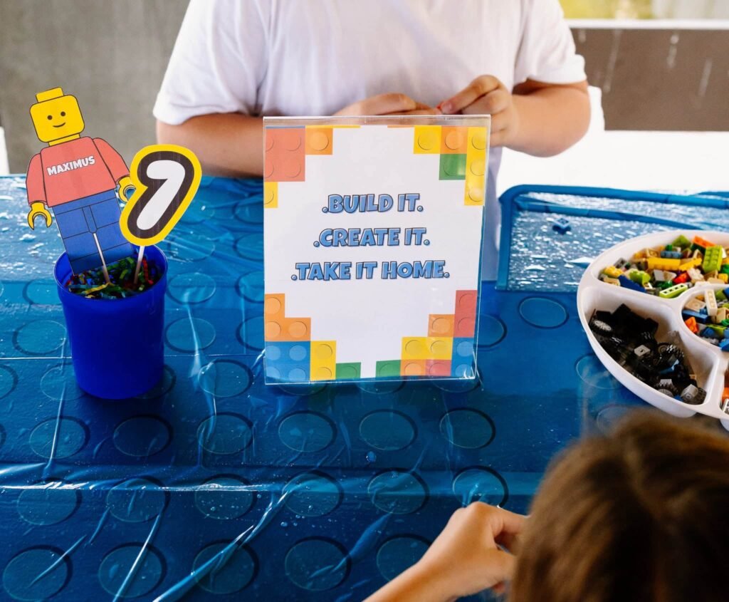 LEGO build station sign on a blue table with bricks in a tray