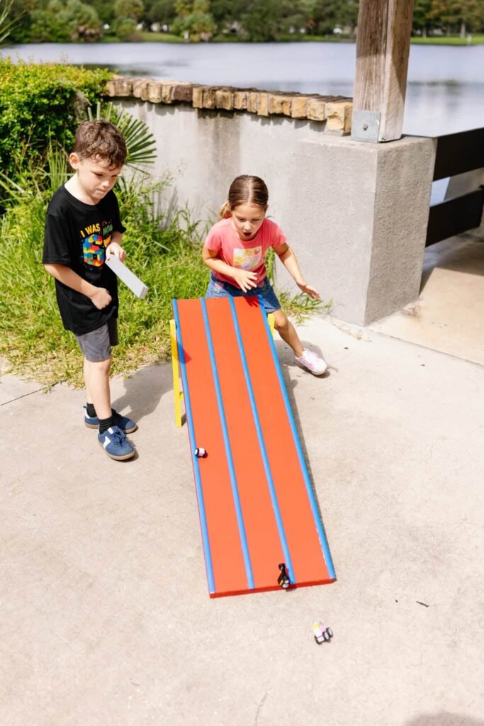 Kids racing toy cars down a wooden ramp at a park