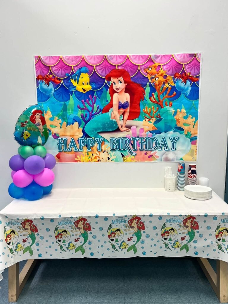 Under the sea backdrop with Ariel above a cake table