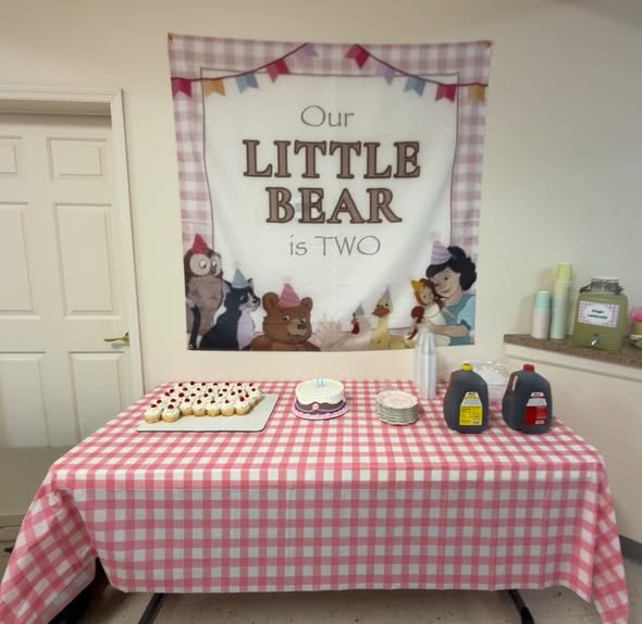 Our Little Bear Is Two banner over a pink gingham dessert table with cupcakes