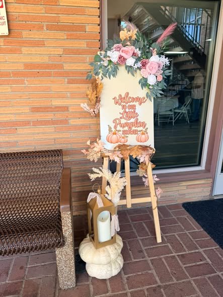 Little pumpkin baby shower welcome sign with pink flowers on an easel