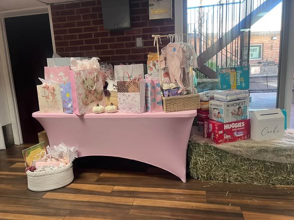 Pink baby shower gift table with gift bags and a hay bale