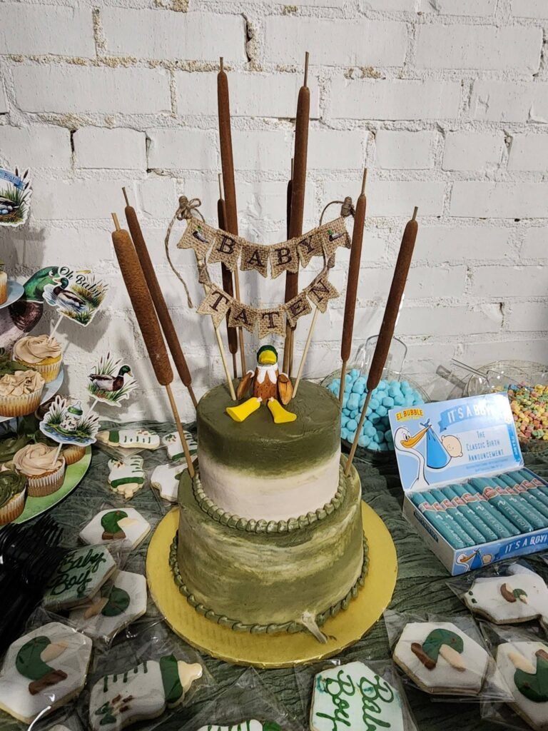 Two tier green baby shower cake with a duck topper and cattails