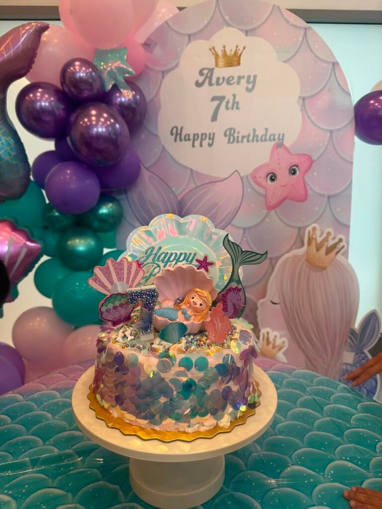 Mermaid tail birthday cake in front of a purple happy 7th birthday sign