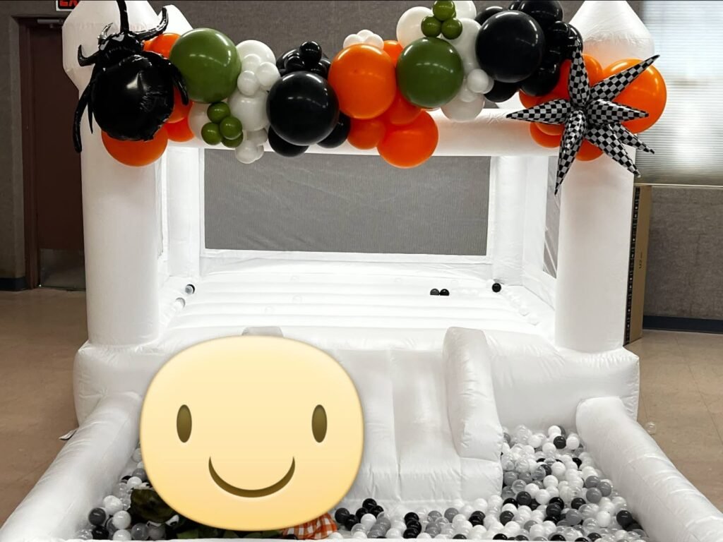 White bounce house with orange, black and green balloons