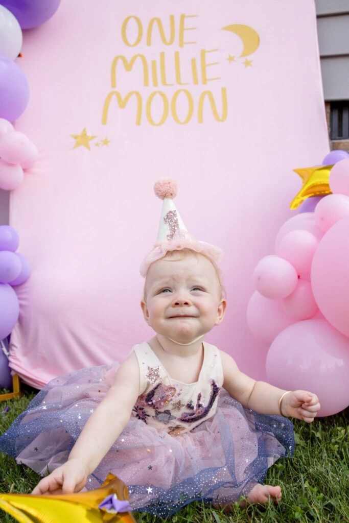 Baby girl in a party hat and tulle skirt by a One Little Moon sign
