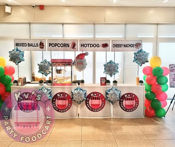 Row of snack stations for mixed balls, popcorn, hotdog and nachos with red and green balloon columns