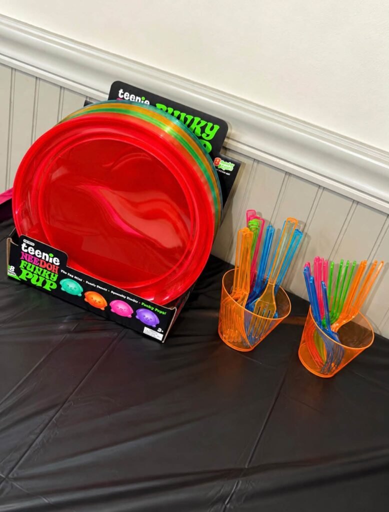 Red plates with neon cups and straws next to a Nee Doh box