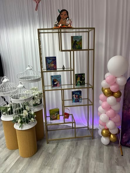 Gold shelf with storybooks and decor next to a pink and gold balloon column