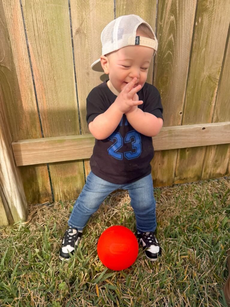 Toddler in a cap with a red ball in the yard