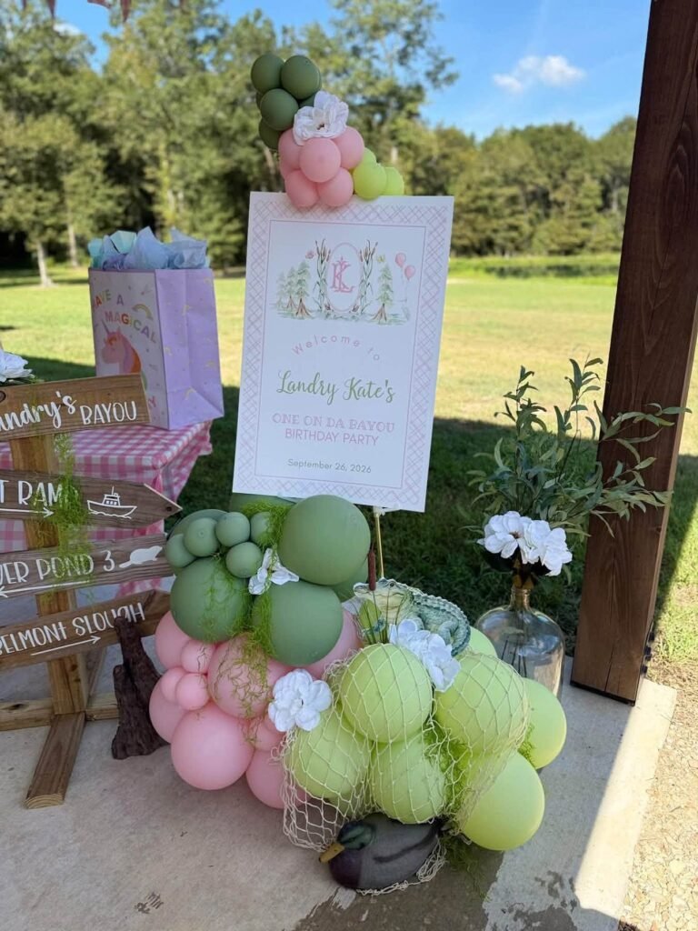 Pink and green balloon cluster by a welcome sign at a bayou birthday party