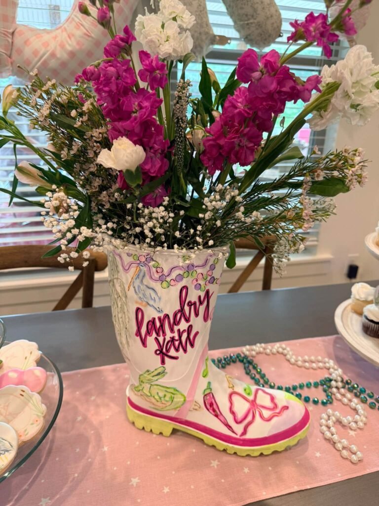 Painted rain boot vase with pink flowers and Mardi Gras beads on a party table