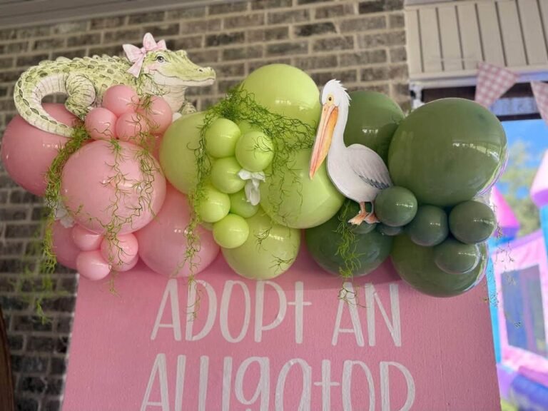 Close up of an Adopt an Alligator sign with pink and green balloons, an alligator and a pelican
