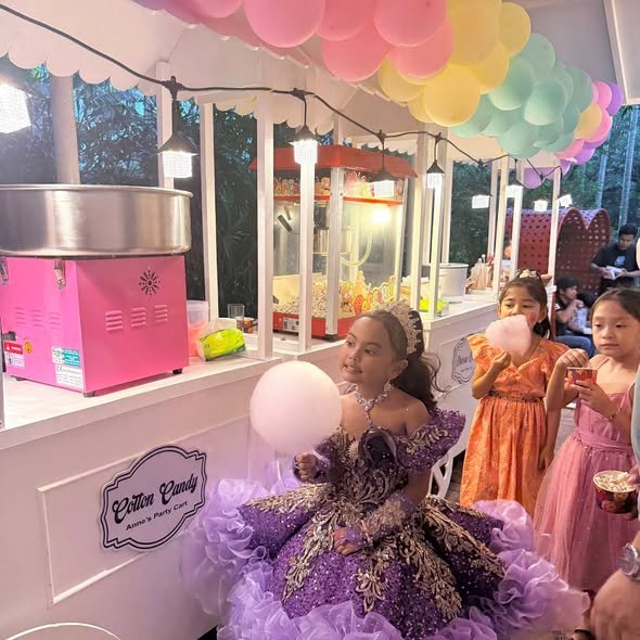 Birthday girl in a purple gown eating cotton candy by a cotton candy cart