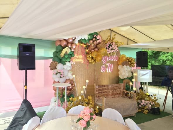 Floral and balloon backdrop with a name sign, lights and a speaker on a stand