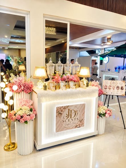 Perfume bar with pink flowers, a gold sign and a menu on an easel