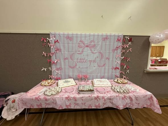 Pink bow baby shower dessert table with a striped backdrop and satin bows