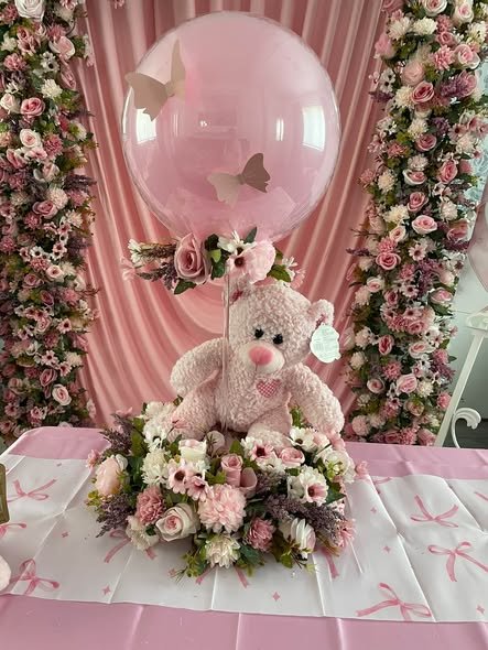 Teddy bear in a bed of pink flowers under a clear balloon at a baby shower